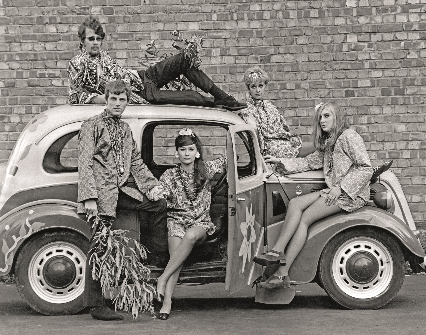 circa 1968:  Young men and women pose in and on a car  while modeling factory-made versions of Flower Power clothing, England.  (Photo by Brian Duff/Daily Express/Express/Getty Images)